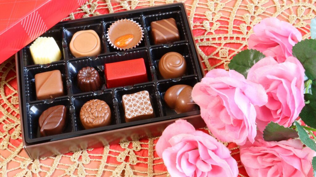 ギフトボックス入りのチョコレートとピンクの花が並ぶ、アムール・デュ・ショコラを想わせる華やかなイメージ写真