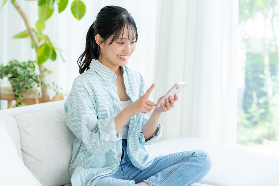 明るい部屋でスマートフォンを操作する女性の写真