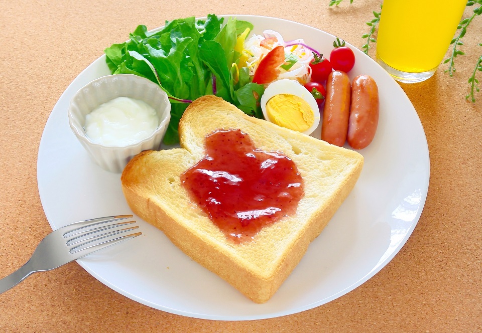 ジャムトーストとゆで卵、ソーセージ、野菜、オレンジジュースの朝食プレート（米粉パンのイメージ）