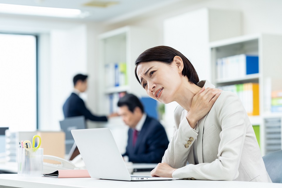 肩こりに悩みながらデスクワークをする女性