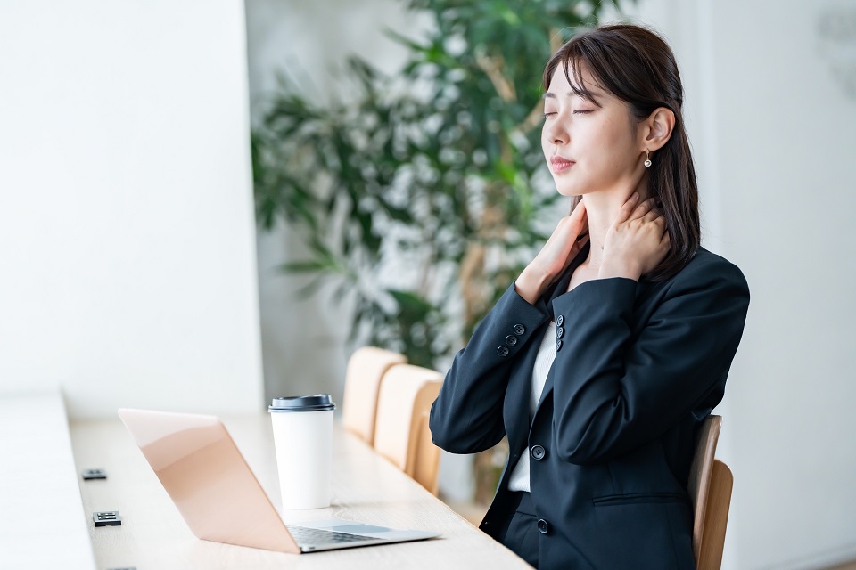 肩こりに悩みながらデスクワークをする女性